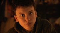 a young boy in a green hoodie staring at the camera